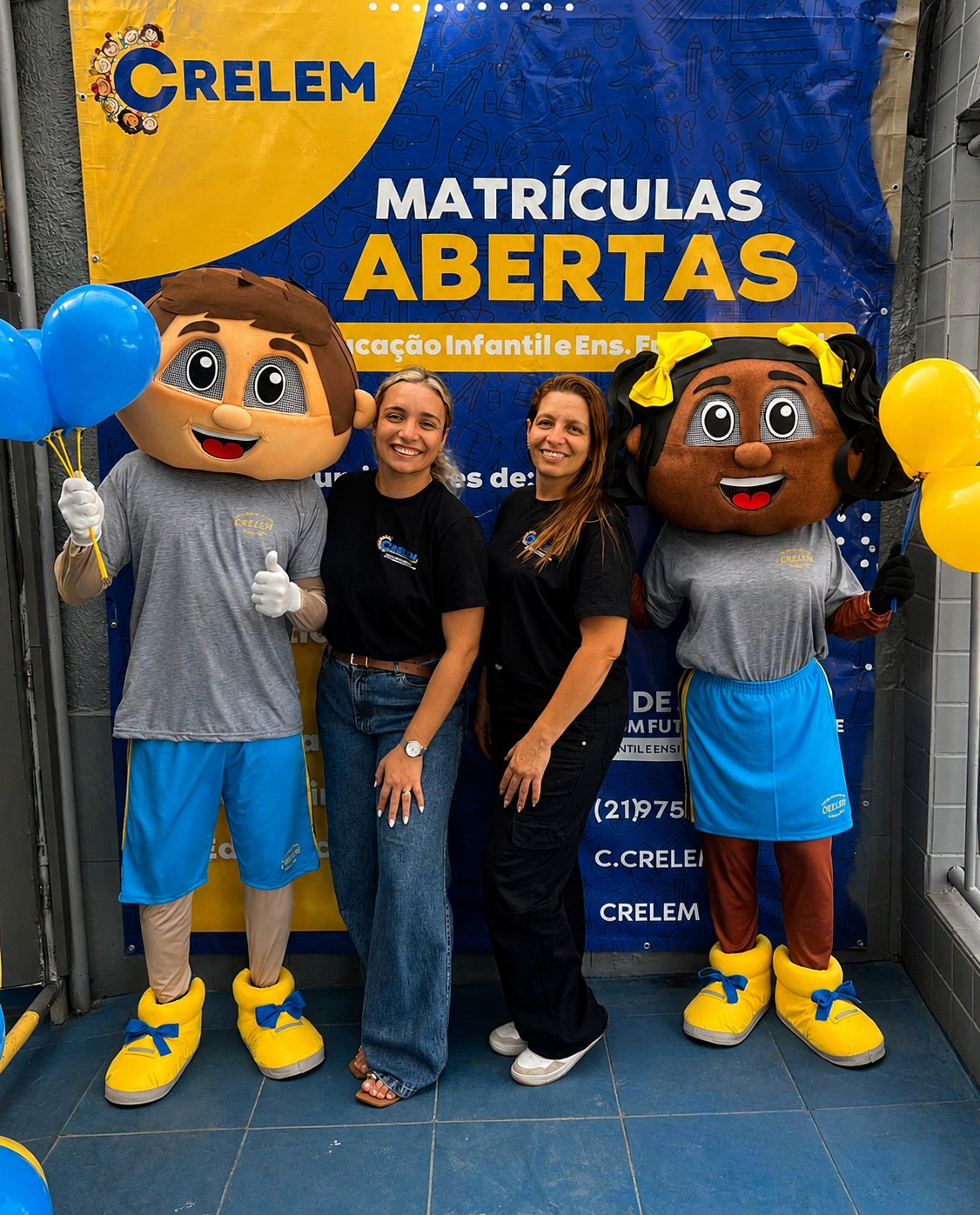 Diretoras da CRELEM com os mascotes da escola na entrada, banner de Matrículas Abertas